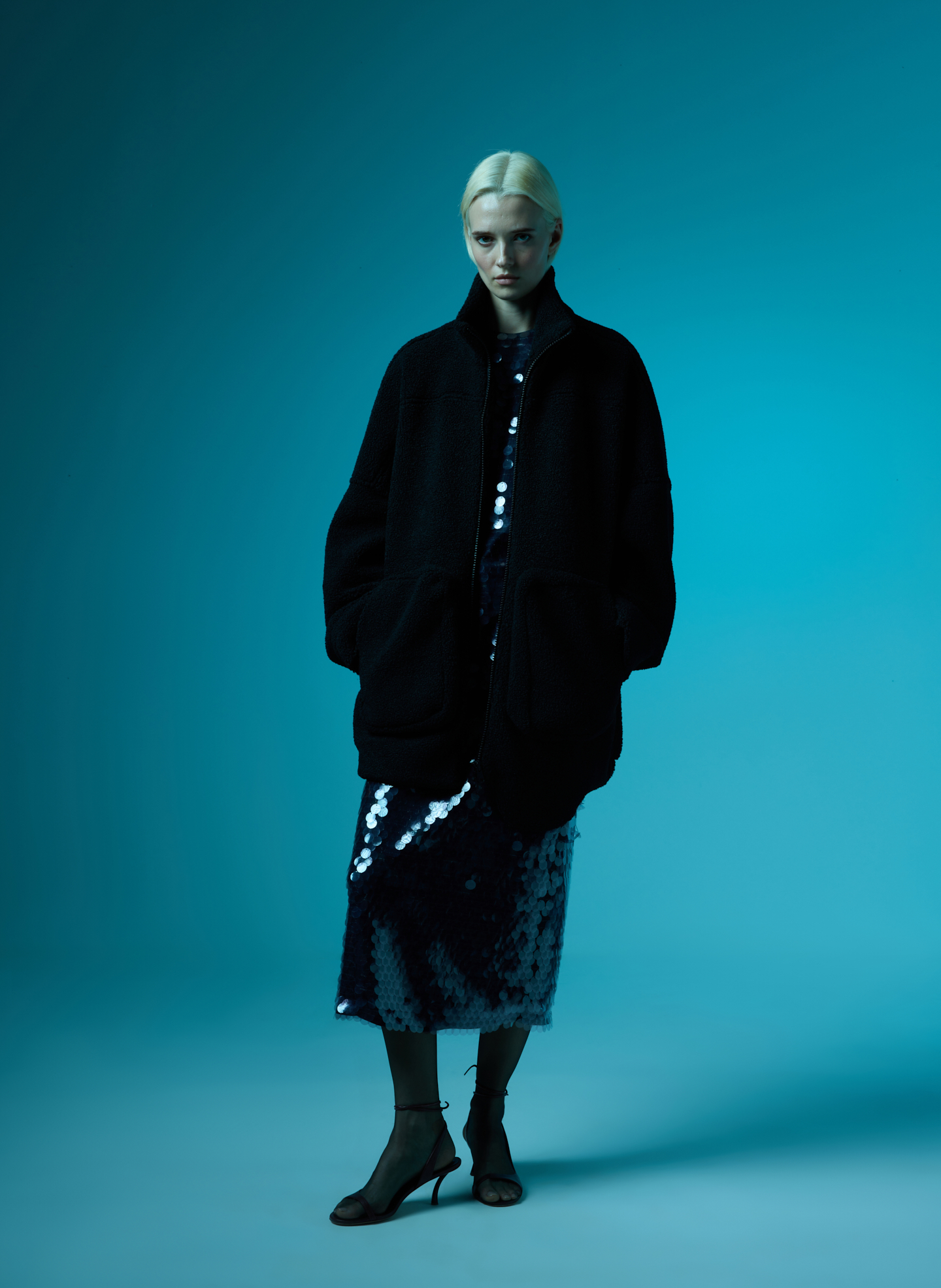Model in stylish outerwear against a blue background, showcasing a fashionable ensemble.
