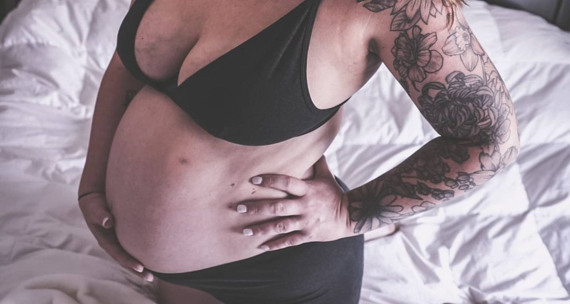 A pregnant woman wears maternity bras, cradling her bump on a bed, wears a triangle bralette from WAMA underwear, one of the best maternity bras.