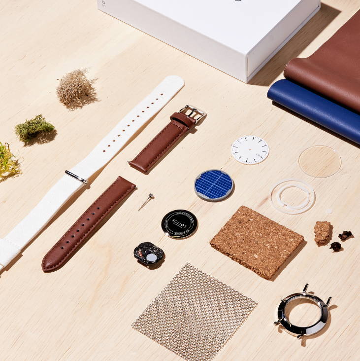Flat lay of Solios watch cases, straps and natural materials on a wooden surface
