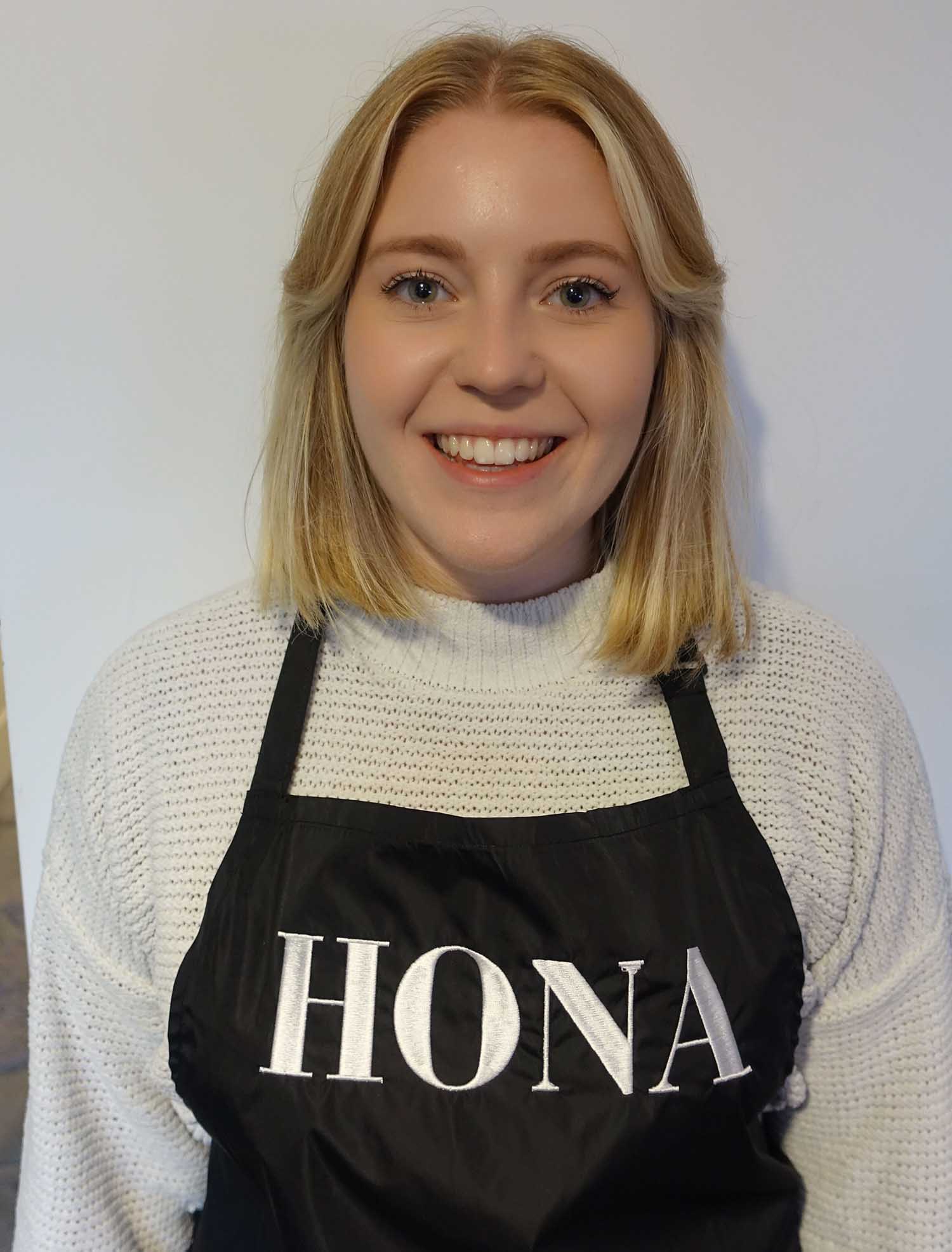 Smiling person wearing a black apron with the word 