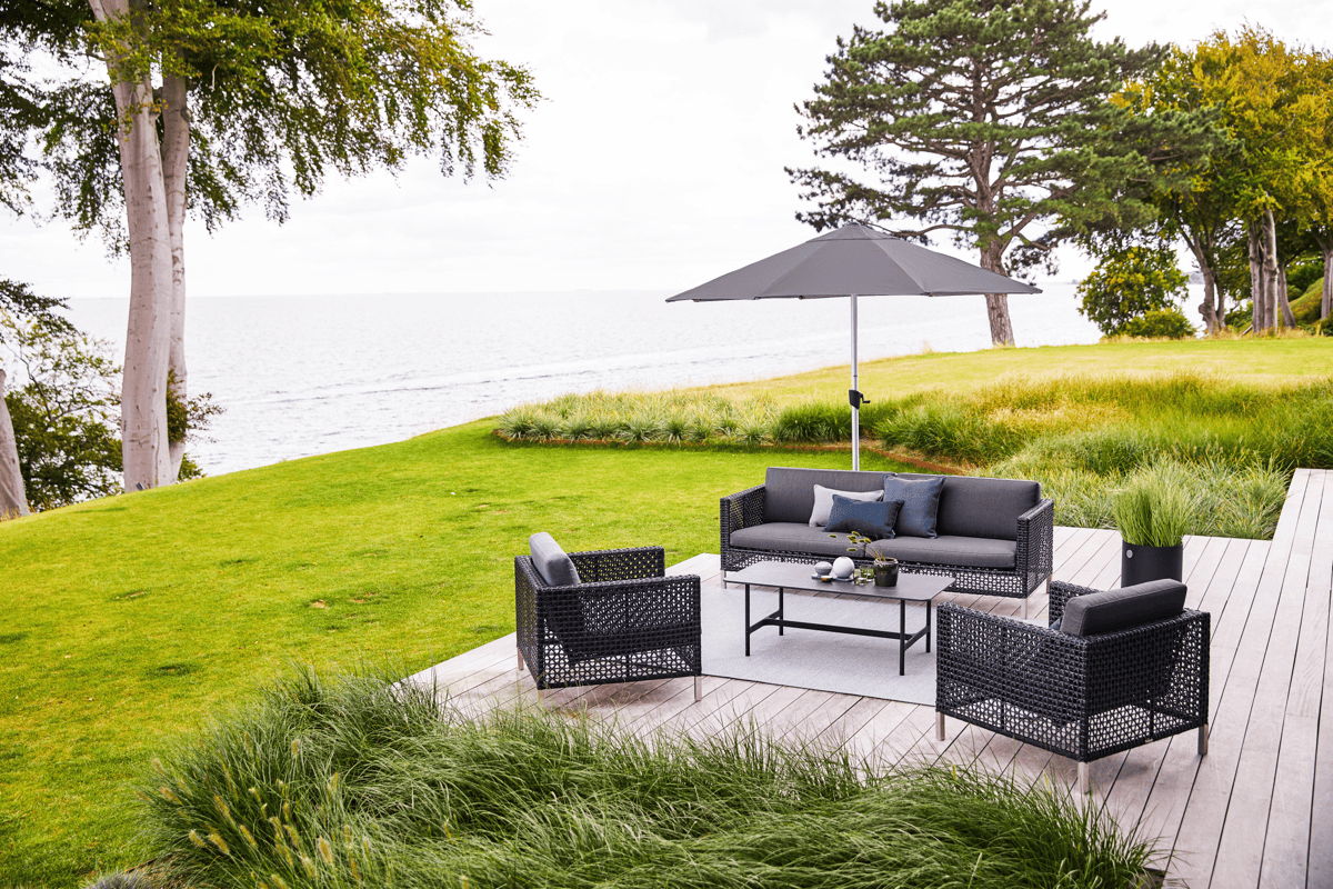 Outdoor lounge set with sofa and chairs under a large patio umbrella on a deck overlooking the ocean.