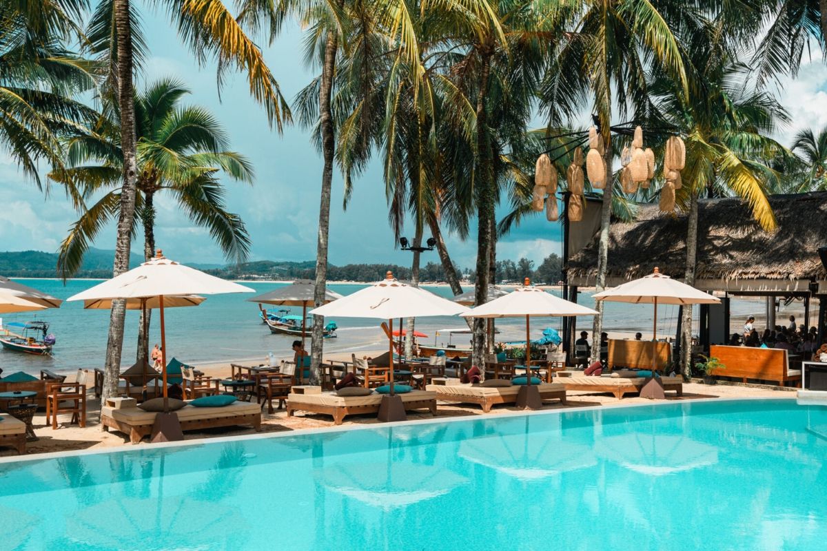 Tropical resort poolside with sun loungers and umbrellas by the beach.