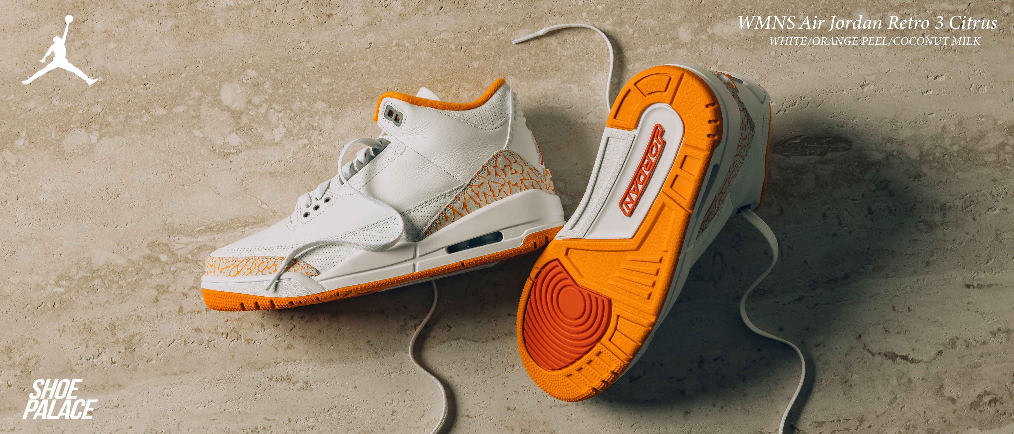 Sneakers in white and orange on a textured surface.