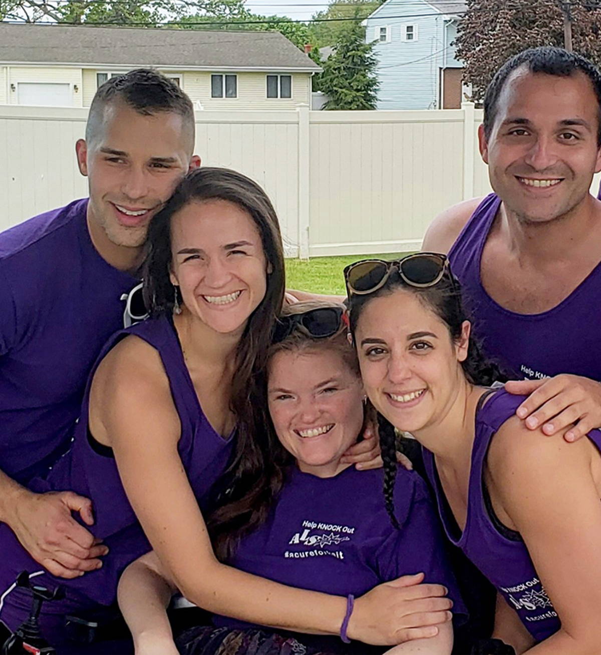 A young woman with ALS and her friends huddled together in matching purple t-shirts. 