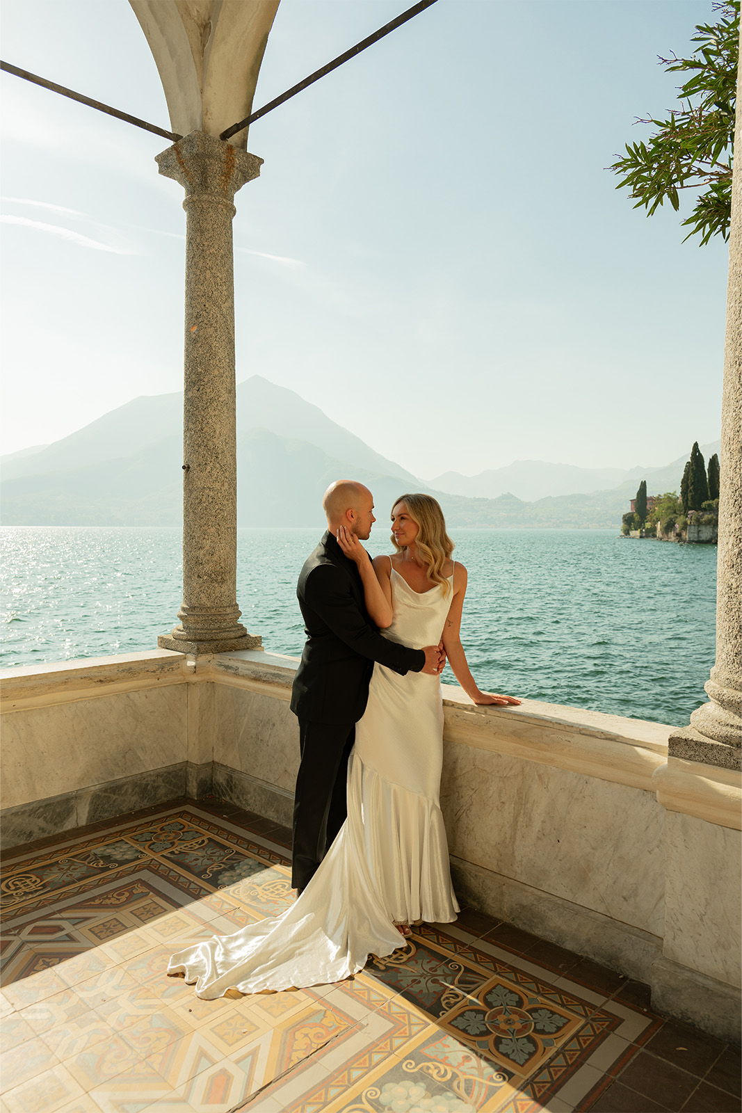 A couple in wedding attire by a serene lakeside.
