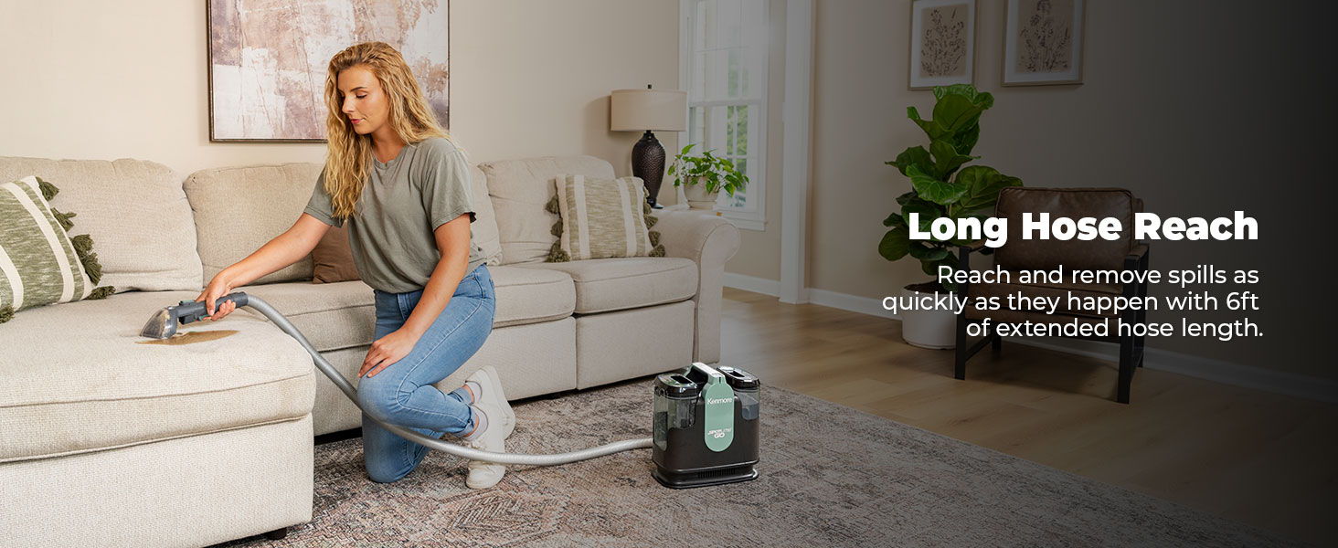 Person vacuuming a couch with a long hose vacuum cleaner.