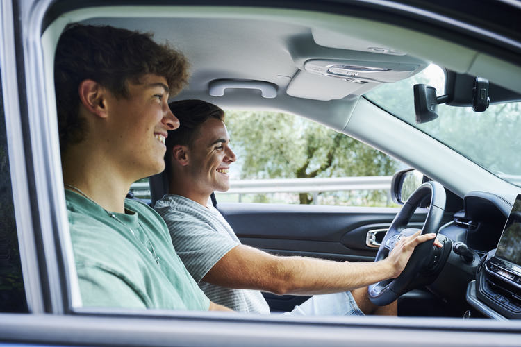 Two young men smiling inside a car, enjoying a drive together.