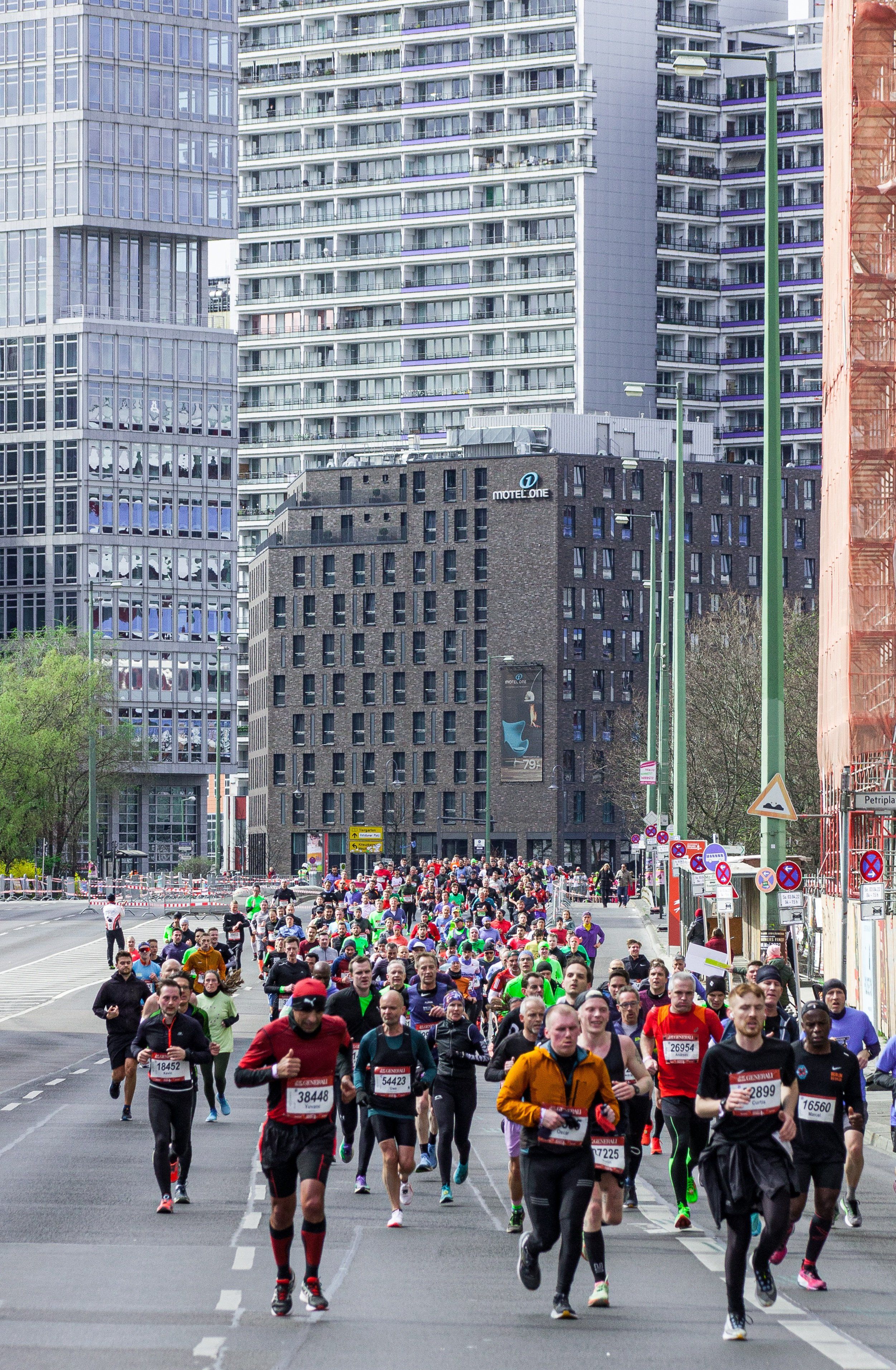 Eine Gruppe von Marathonläufer läuft auf einer Straße durch eine Stadt und wird dabei frontal fotografiert.