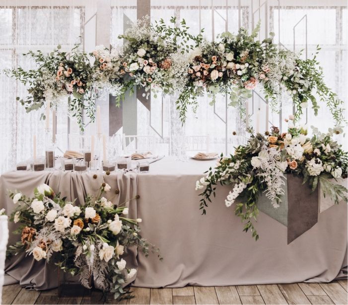 Gray sweetheart table with lush white and peach floral arch and greenery for wedding reception
