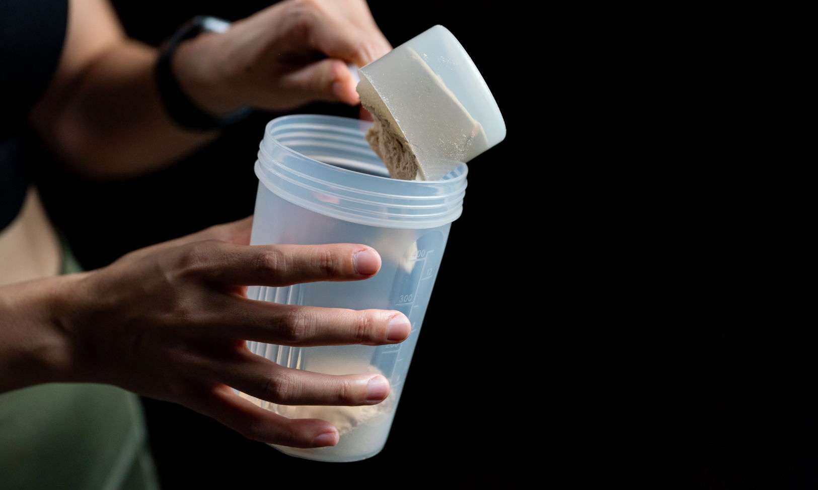 Person holding a scoop above a clear container against a dark background.