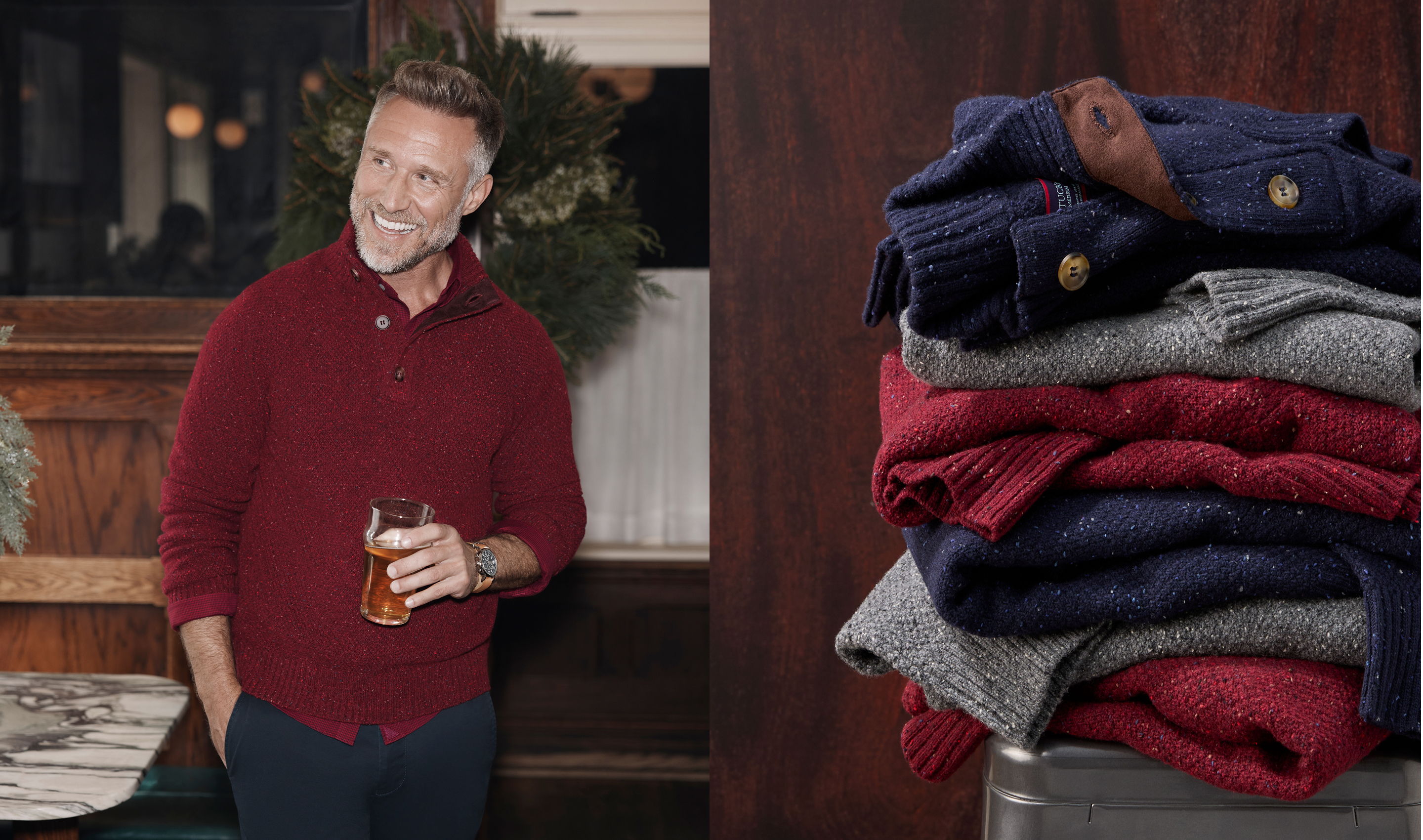 Smiling man in a red sweater holding a drink next to stacked sweaters.
