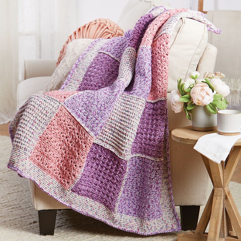 A cozy blanket in pastel purple and pink draped over a chair.