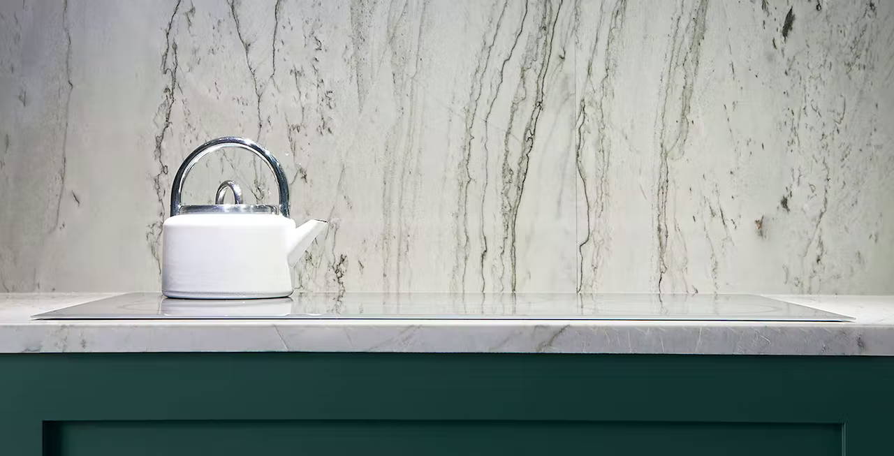 White tea kettle on glass cooktop with marble backsplash
