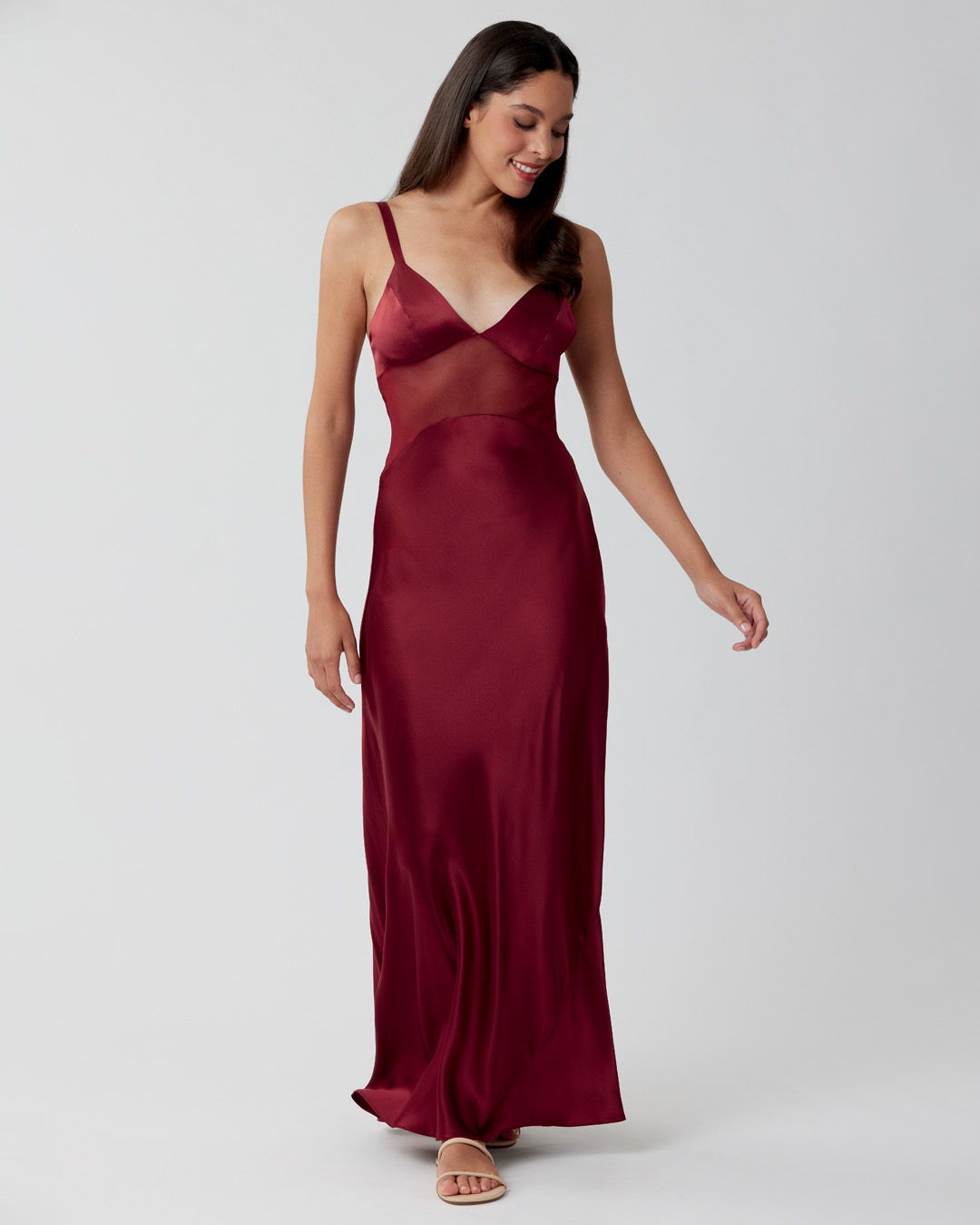 Woman in a burgundy dress walking against a plain background.