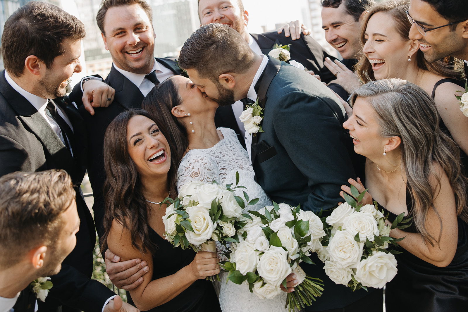 Wedding couple sharing a kiss surrounded by joyful friends and family.