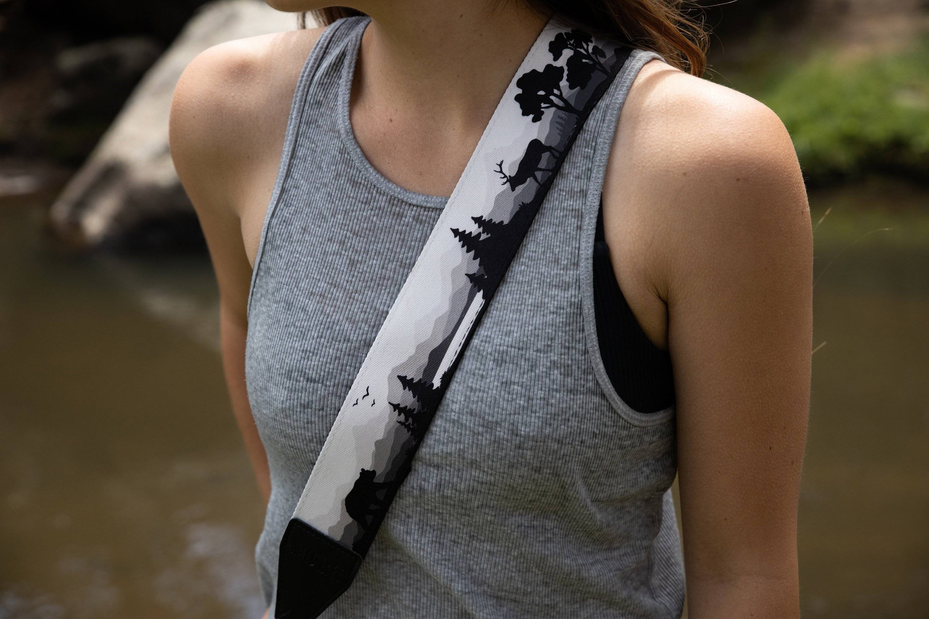 woman wearing a wildlife inspired camera strap design in front of a body of water. 
