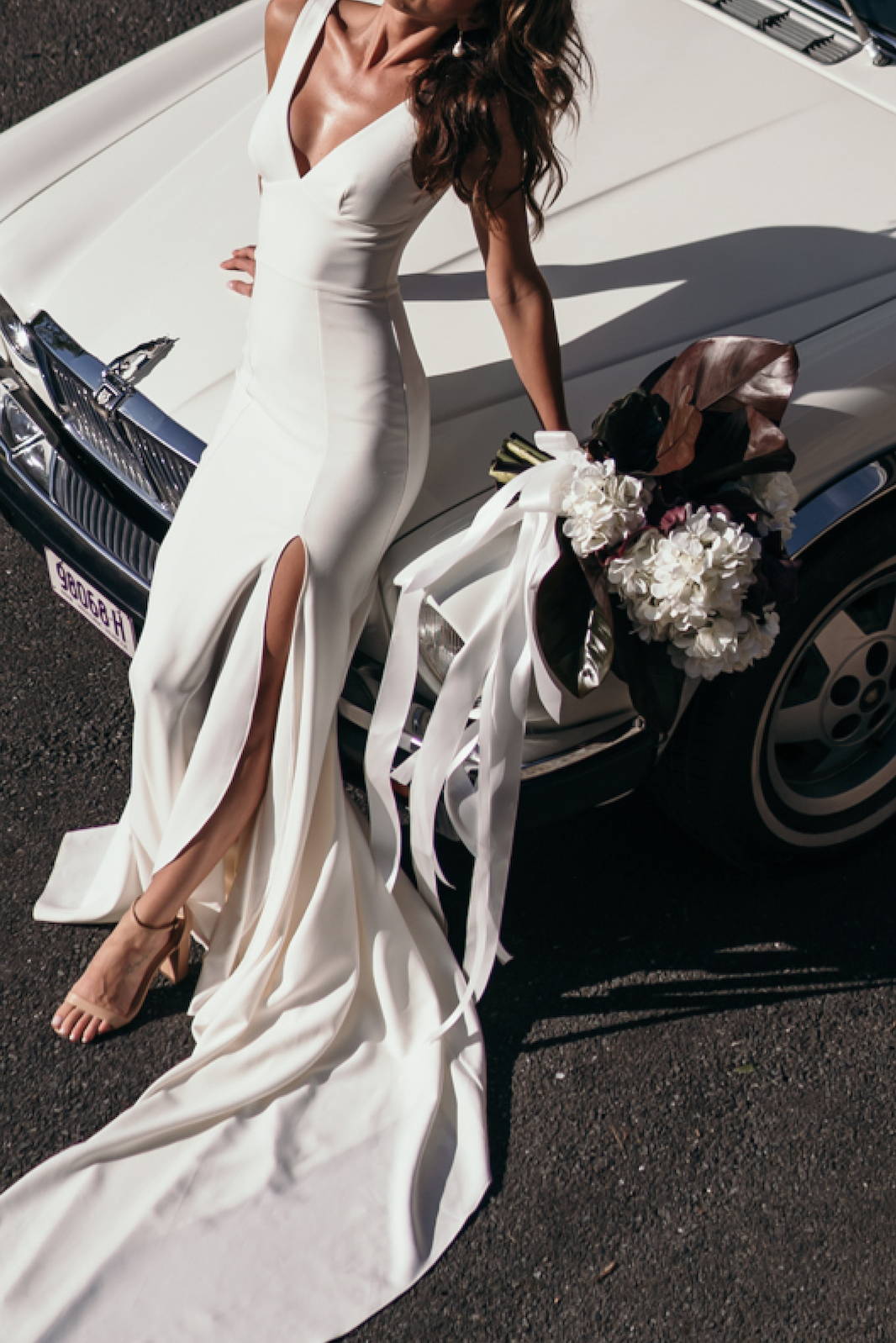 Model sitting on vintage car holding white bouquet of flowers