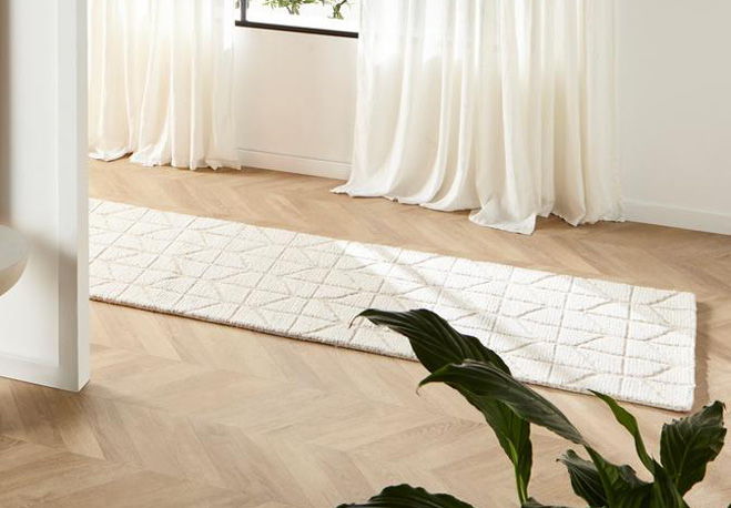 A long, patterned rug on a wooden floor near white curtains.