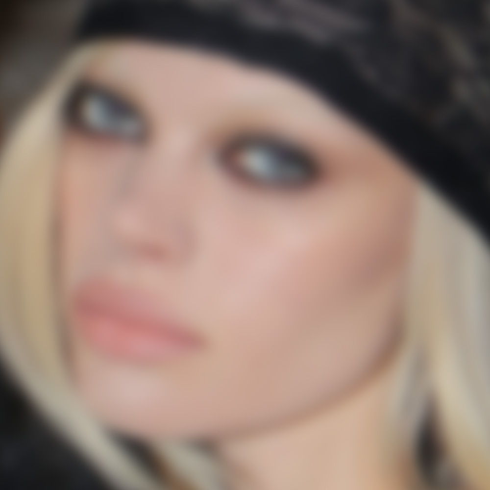 Blurry close-up of a person with light hair and striking makeup.