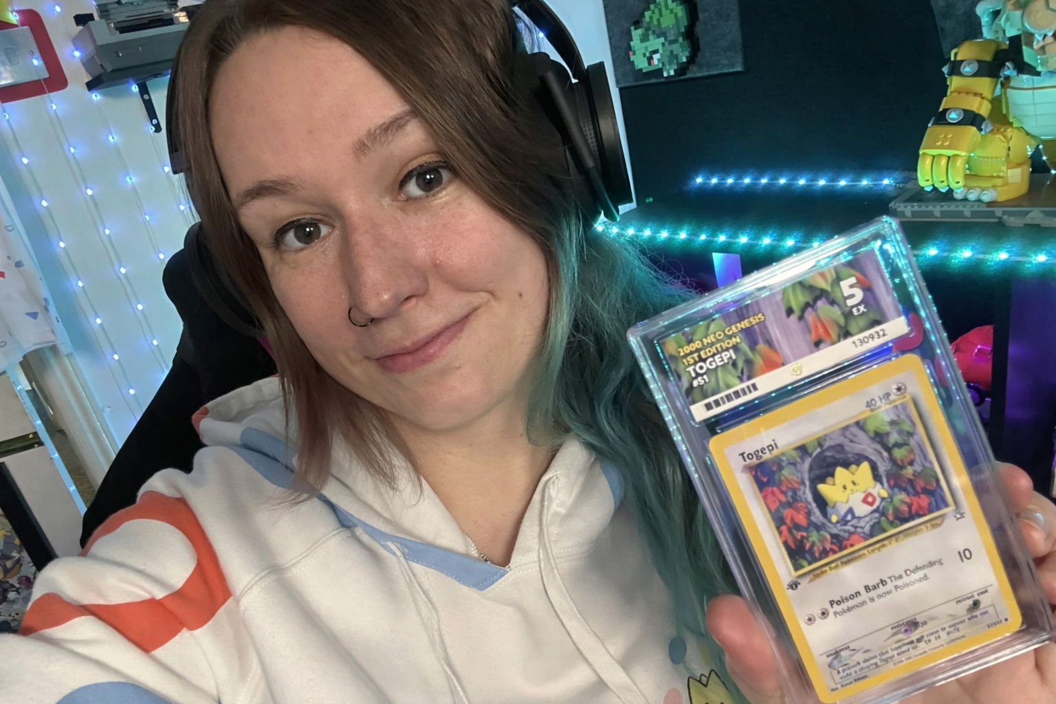 Person holding a Pokémon card, wearing headphones and a hoodie.