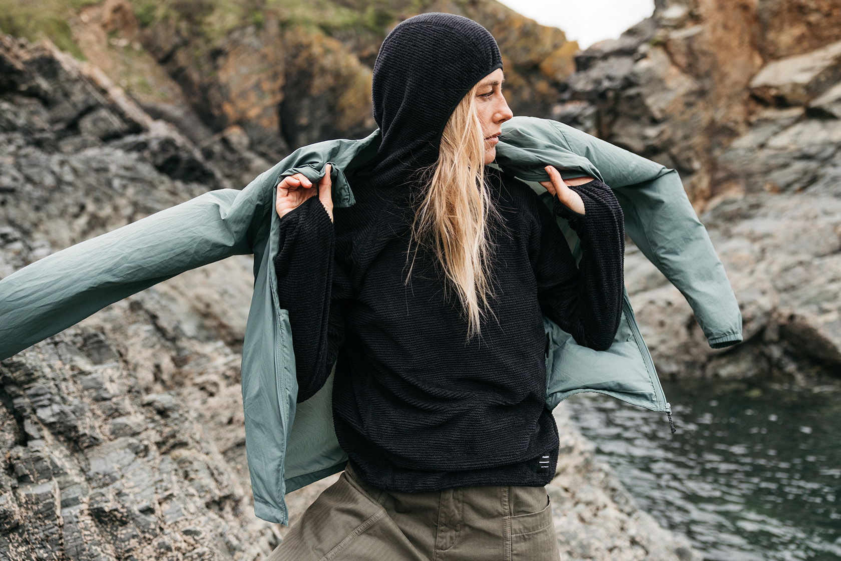 Person in casual clothing standing near water and rocks.