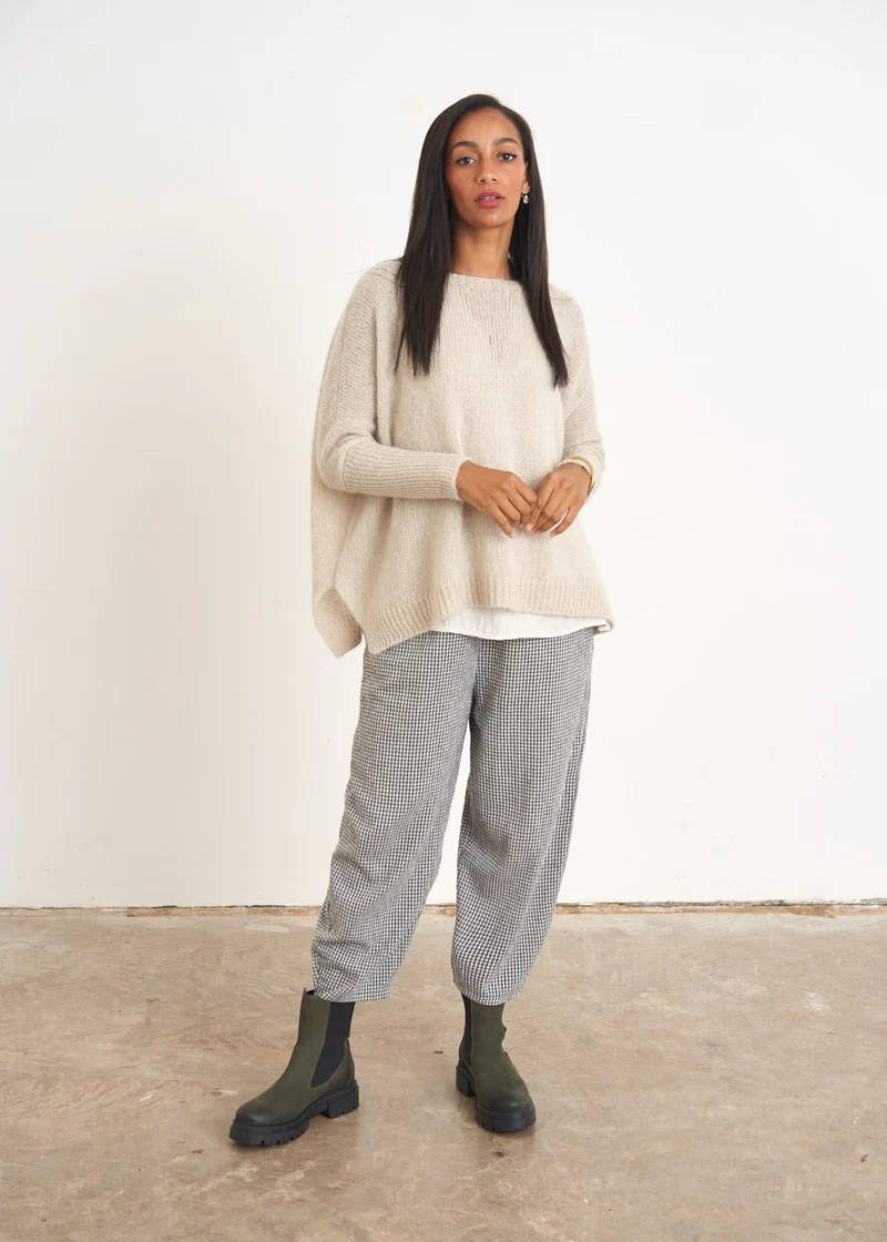 A model wearing an off white, slouchy knitted jumper with fitted sleeves over a white top and grey trousers with green chelsea boots