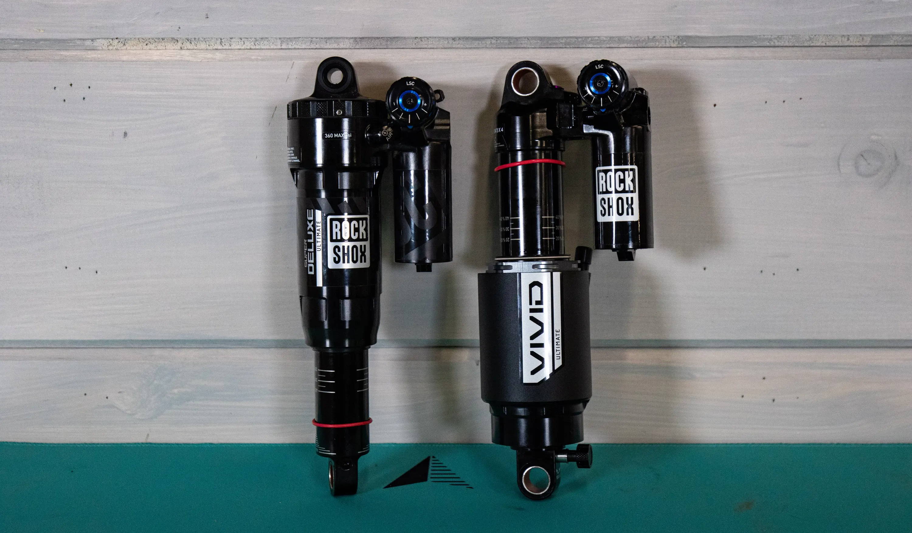 a rockshox super deluxe ultimate and rockshox vivid ultimate rear mountain bike shocks leaning against a white wall 