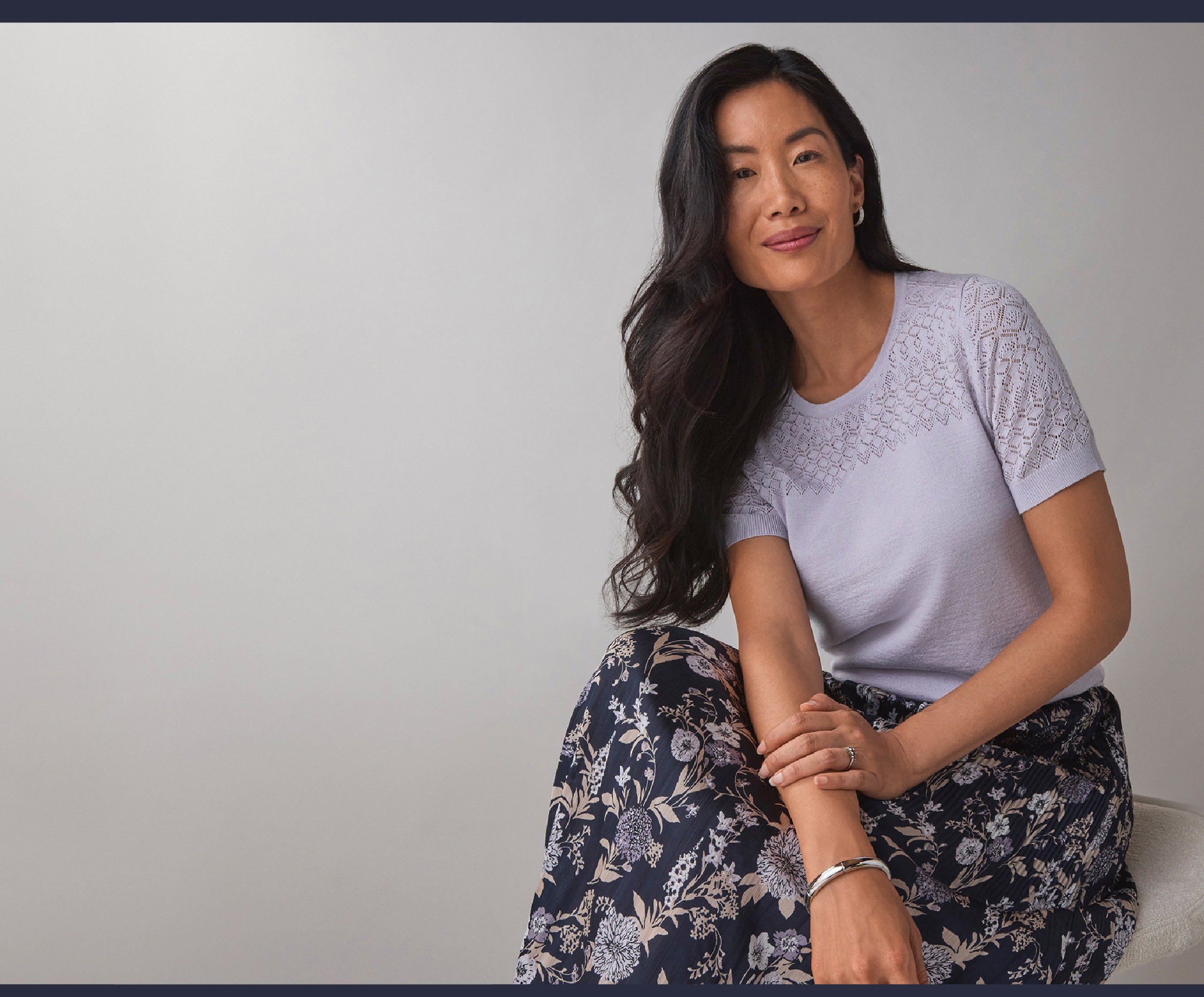 A woman sitting gracefully, wearing a light top and floral skirt.