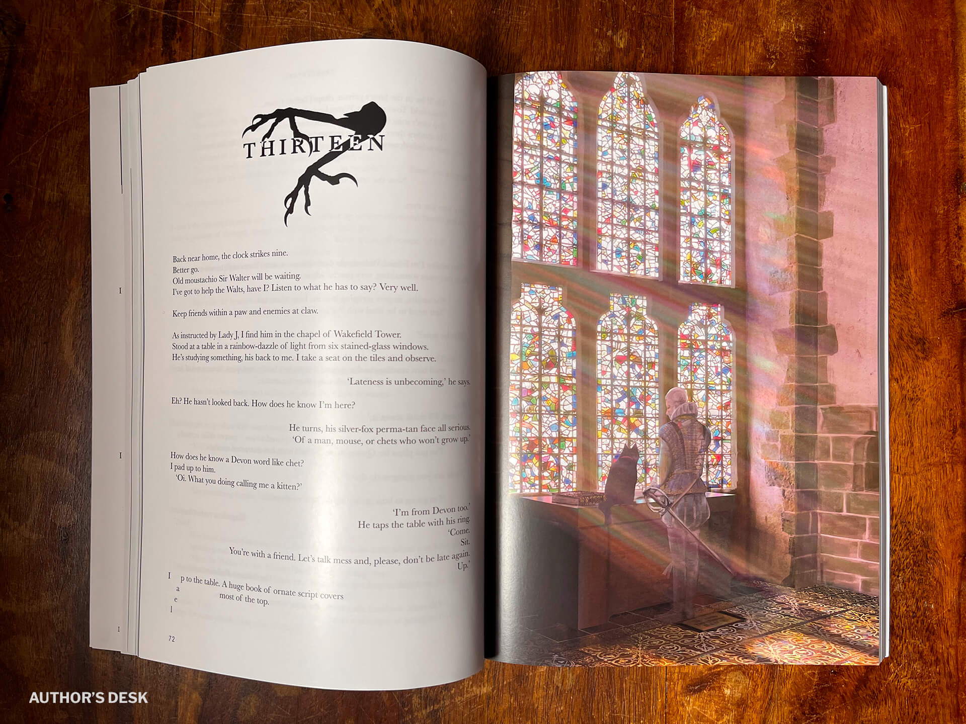 A picture of the open print book showing the start of chapter 13. A pair of raven claws act as the chapter motif on the left page - beneath is the unique text style of the book with Teufel on the left side of the page and his opponents on the right. On the page opposite is a full size picture of Sir Walter Raleigh stood at a table bathed in sunlight from an ornate six panel stained glass window inside Wakefield Tower. On the table is a large book and Thunderpaws