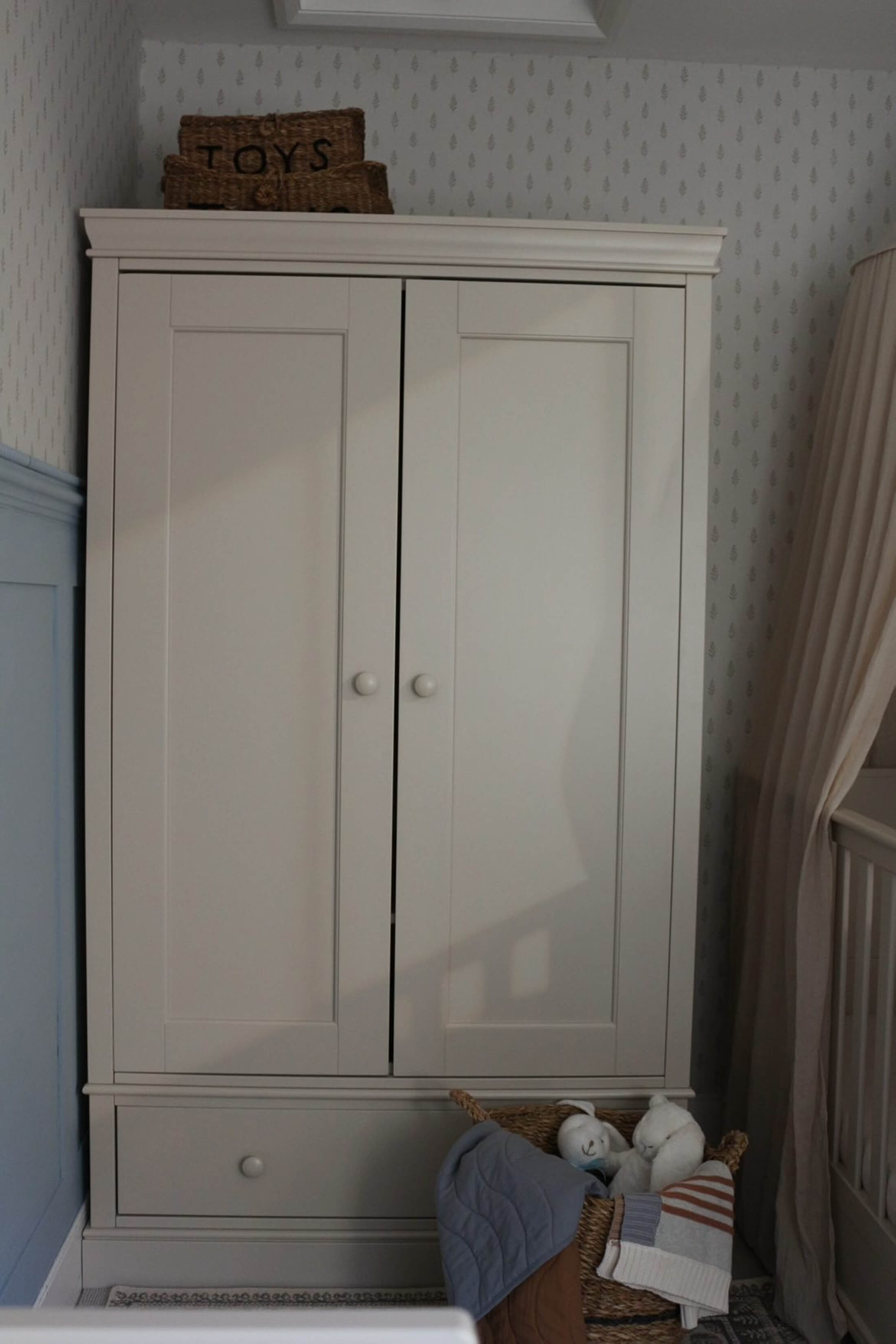 A light-colored wardrobe with a drawer, next to a basket and curtains.