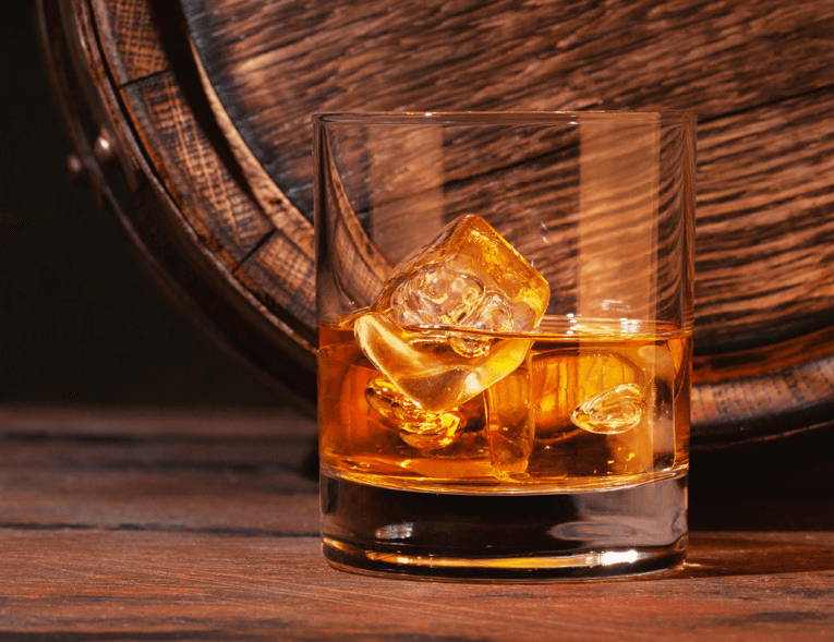 Ein Glas Rum mit Eis vor einem Fass