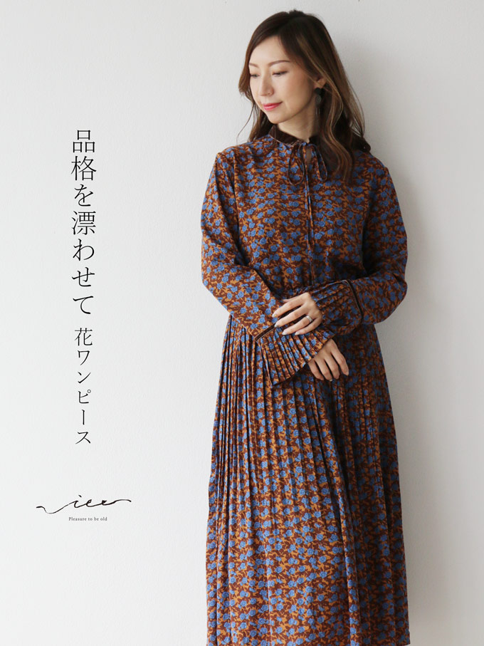 Woman in a patterned dress standing against a white wall.