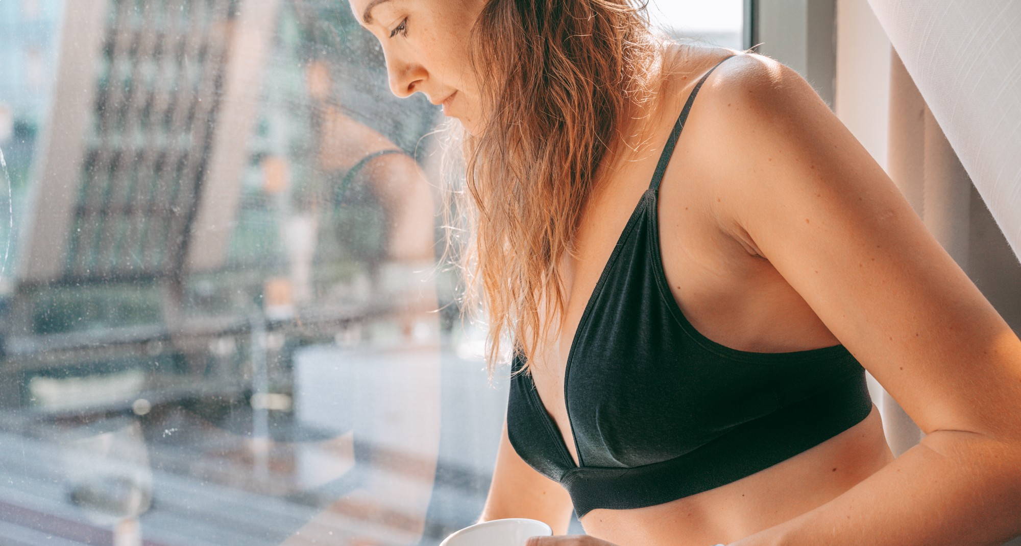 A woman wearing a WAMA triangle bralette looks out the window and wonders how long should a bra last.