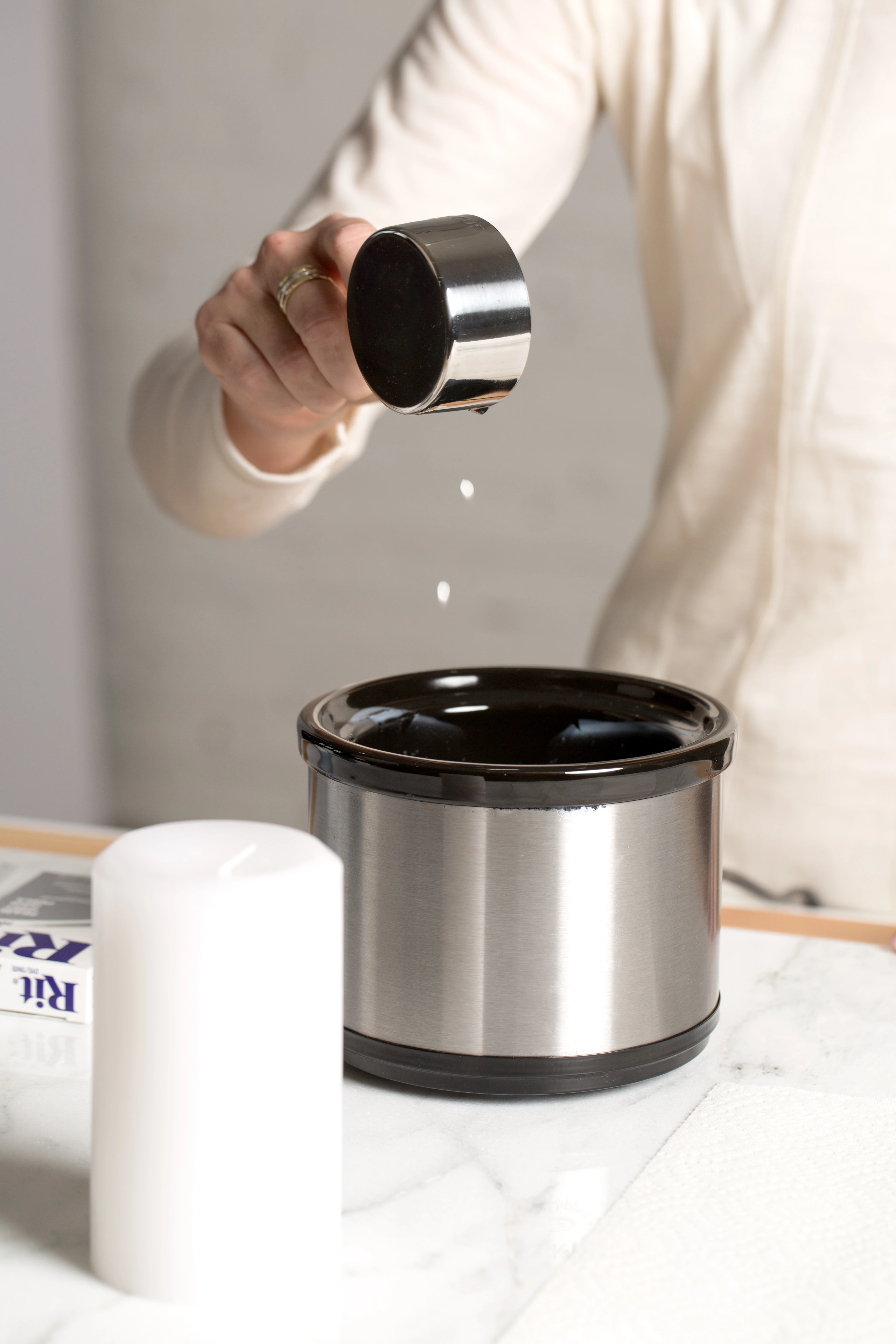 Person pouring sugar into a black and silver slow cooker.