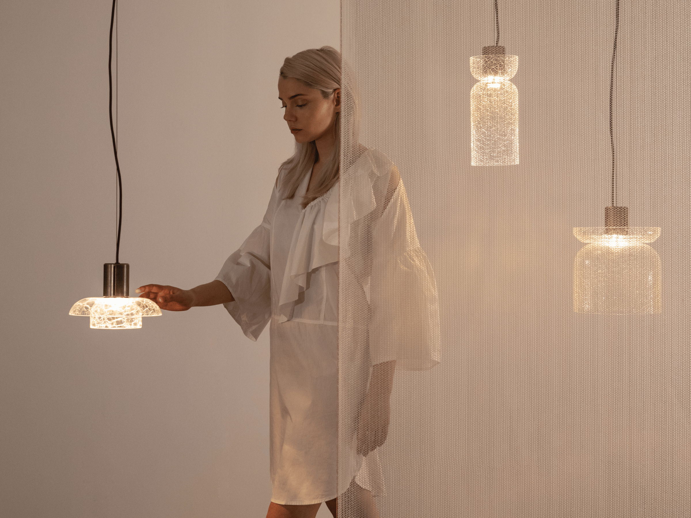 model touching one of 3 crackle glass lighting design pendants hanging from ceiling