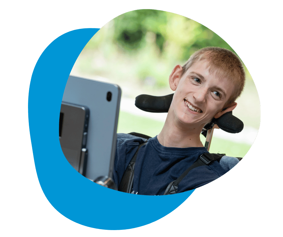 Person using a Grid Pad 16 while smiling, seated in a supportive chair outdoors.