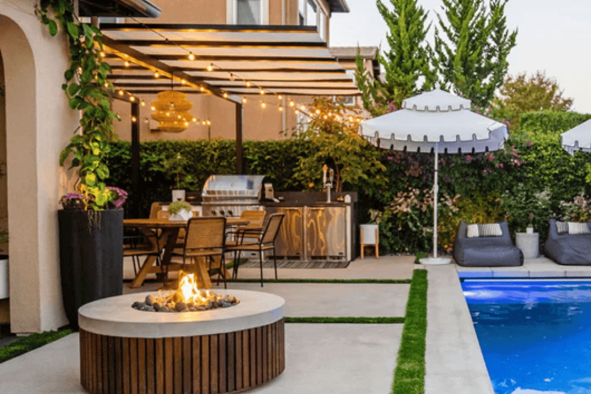 Backyard patio with round outdoor fire pit, pool, umbrella lounge seating, and outdoor kitchen for entertaining.
