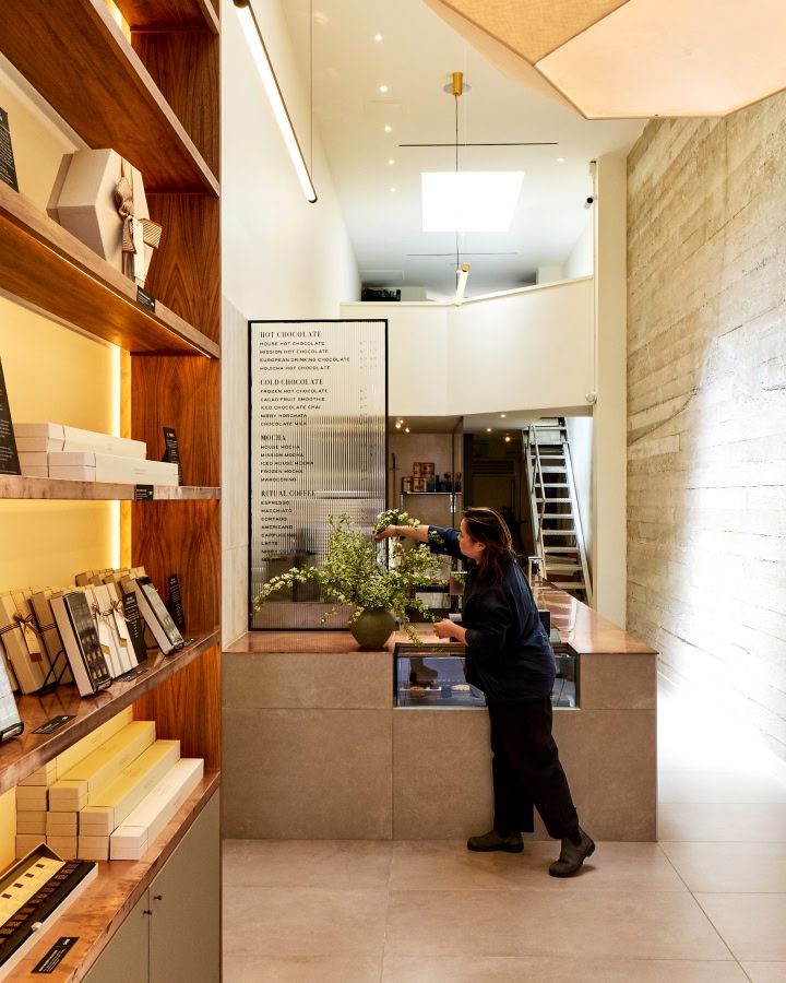 A modern interior with a counter, shelves, and a person tending to plants.