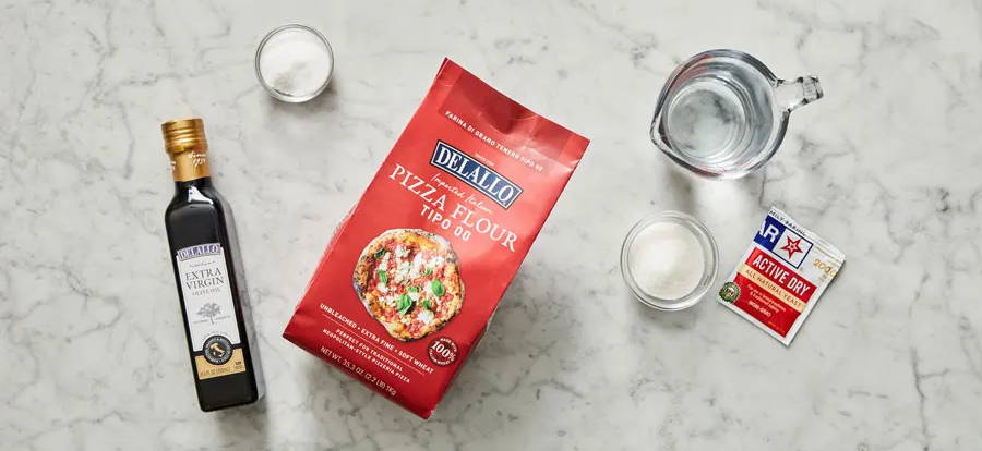 Bag of pizza flour, bottle of olive oil and yeast package on a marble table