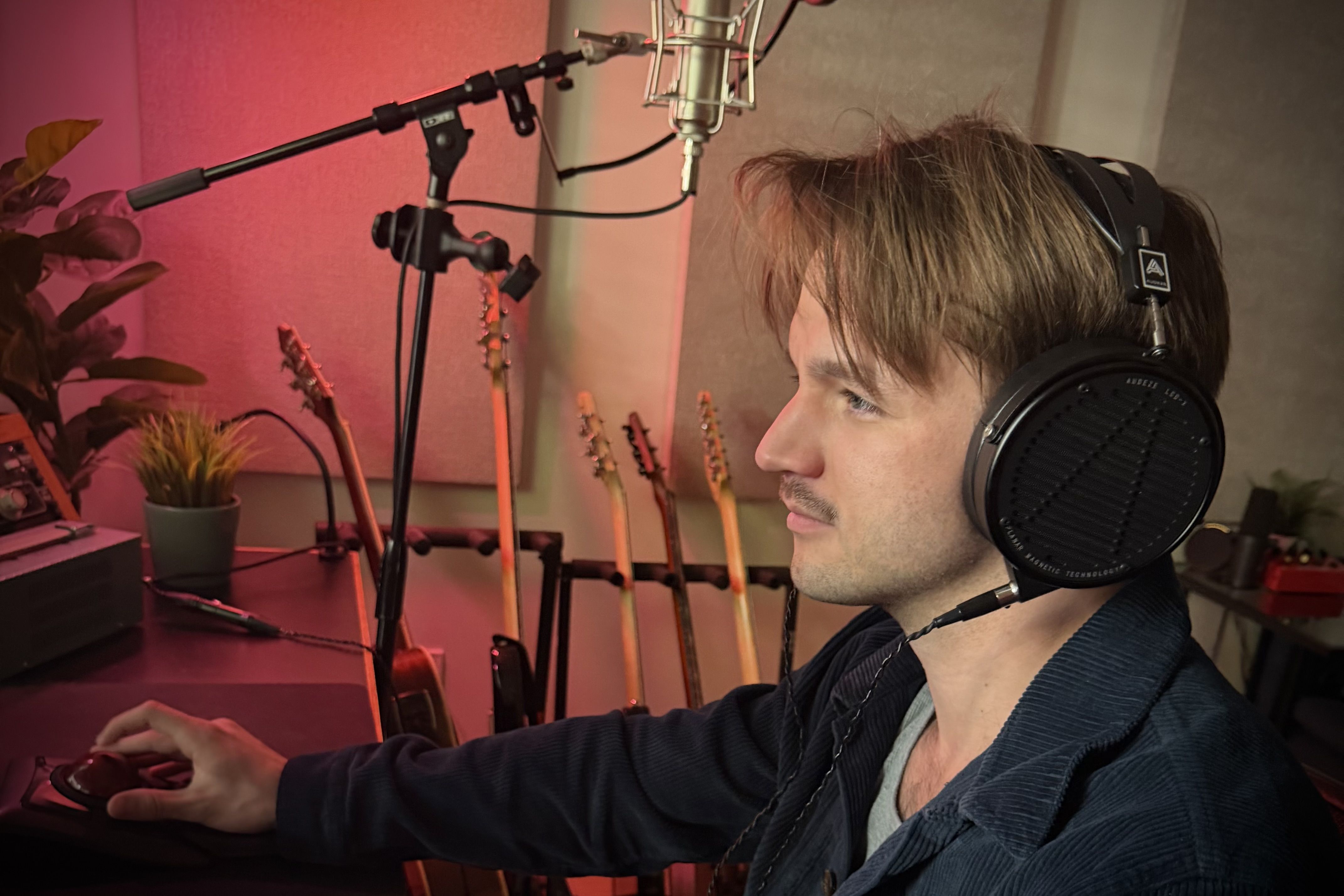 David Kingston wearing headphones in a studio, focused on a computer. Guitars in background.