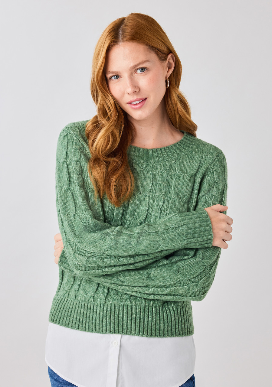 Woman in a green cable-knit sweater, smiling and posing with crossed arms.