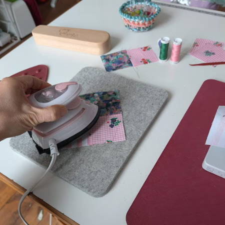 Using a pink mini iron on a mini wool pressing mat next to a sewing machine
