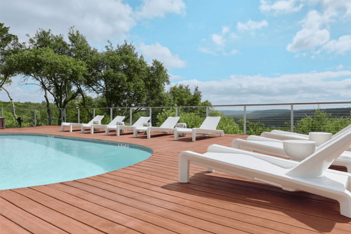 White poolside chaise lounges lined along a curved pool deck with scenic views for resort style poolside design.