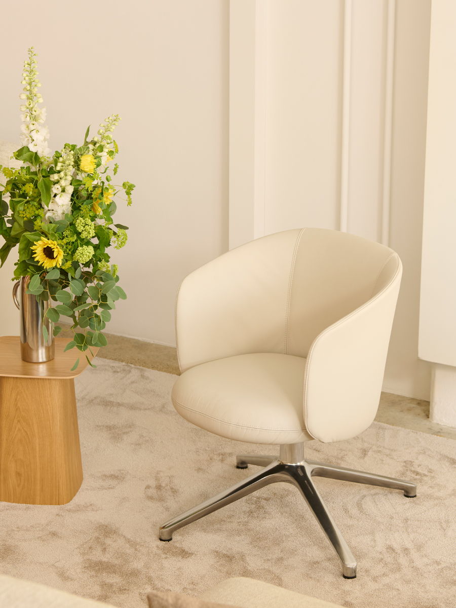 Modern white Mikado swivel chair by Vitra beside a wooden table with a floral arrangement.