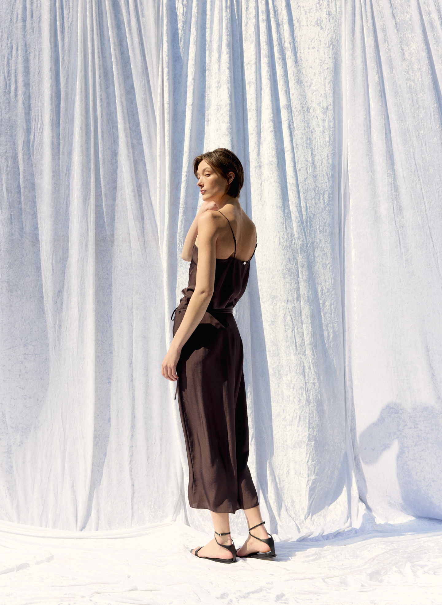Model in a brown dress poses against a white backdrop.