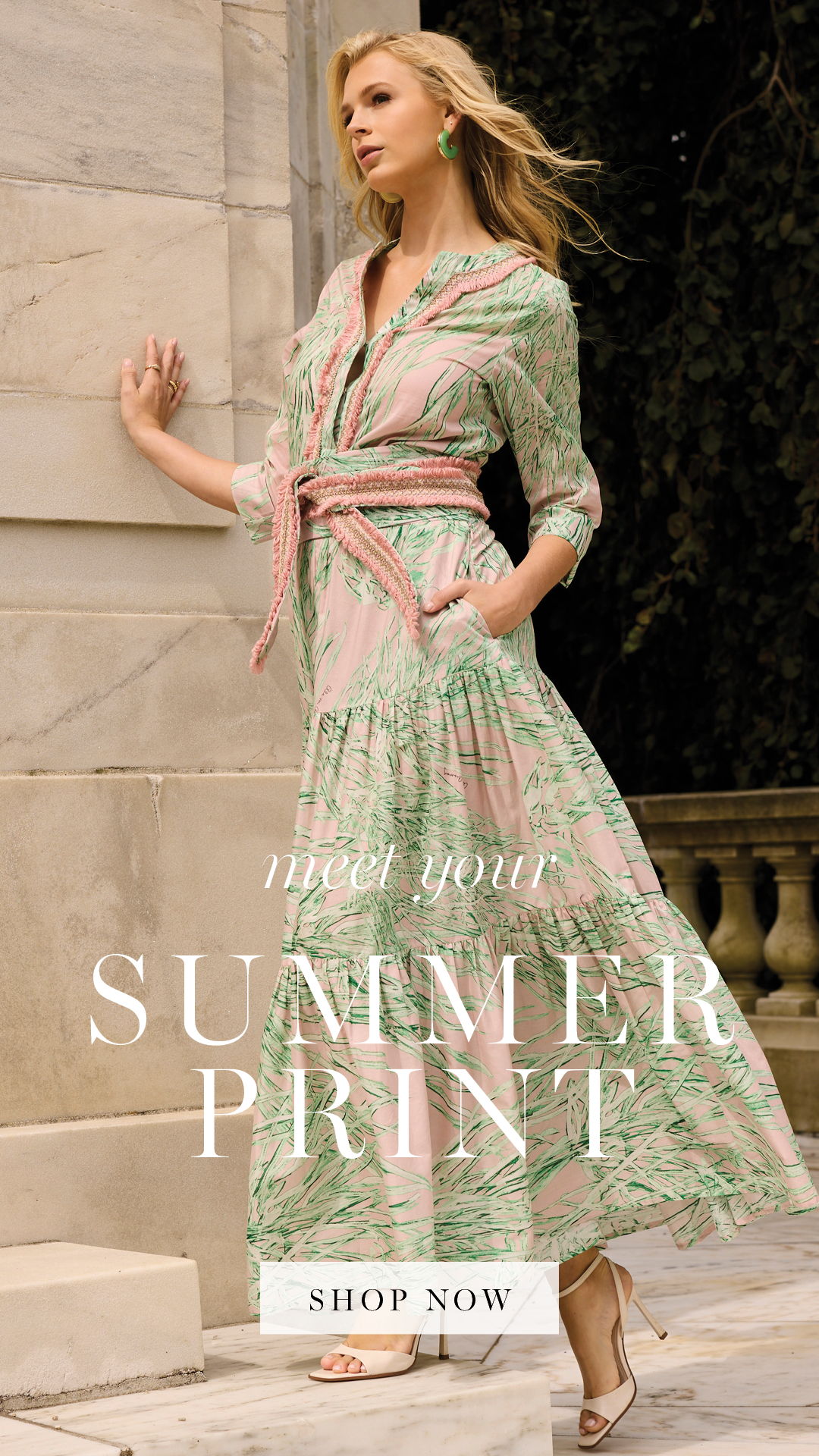 Model showcasing a floral summer dress against a stone background.