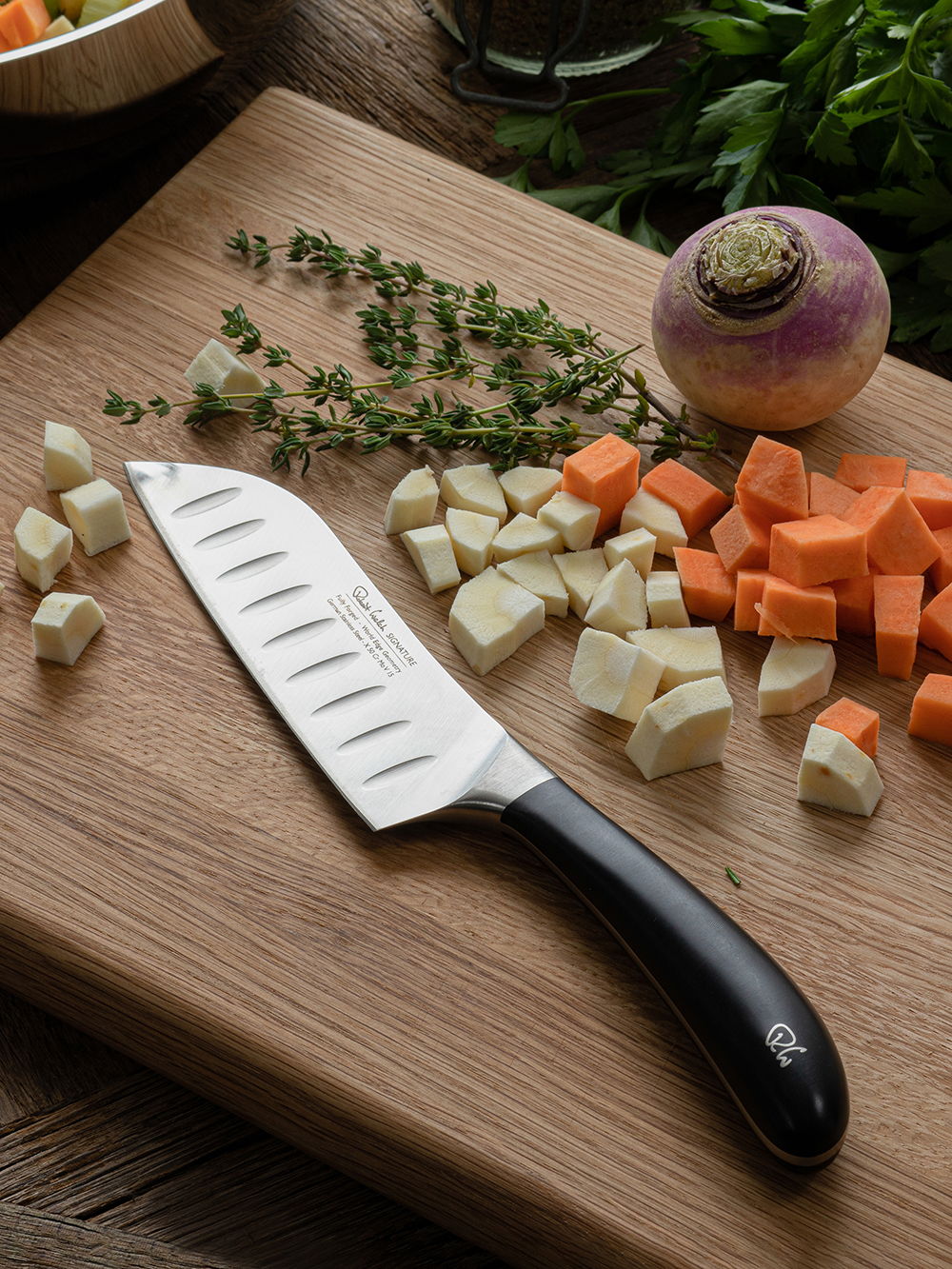 Chopped vegetables and the Signature Santoku knife on a wooden cutting board.