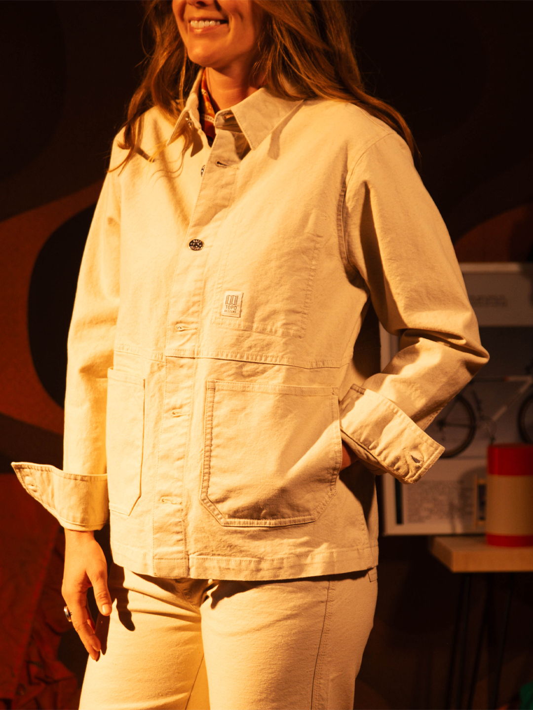 Person wearing a light-colored jacket and pants, smiling in a casual setting.