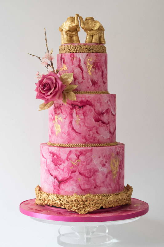 3 tier wedding cake with pink and gold designs and golden elephant statues on the top