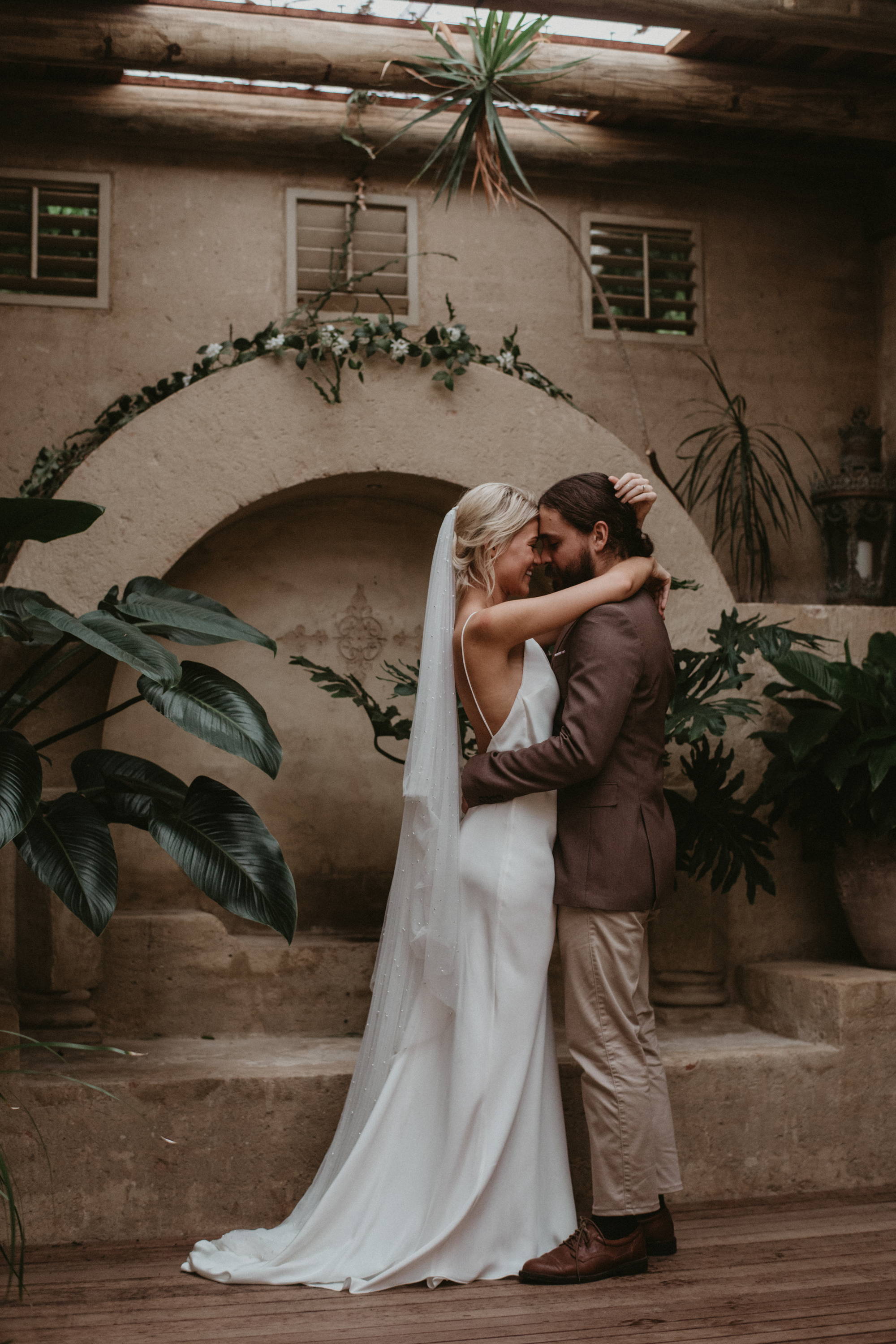 Bride wearing a long tulle veil and silk dress with groom in brown suit